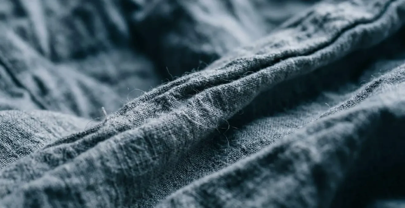 Abstract macro view of crumpled bedsheet fabric in cool tones showing texture and tension, symbolizing sleep difficulty