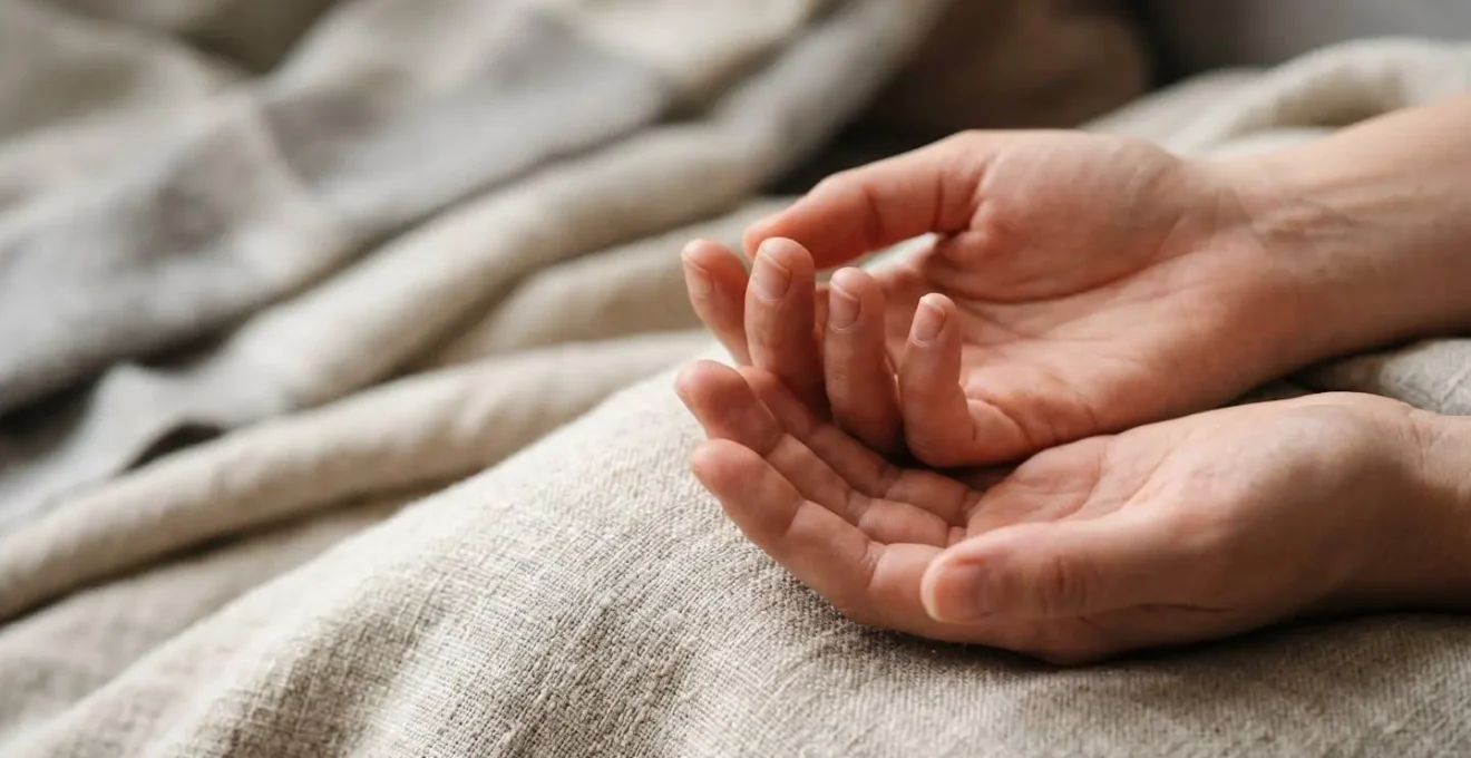 Close-up view of hands resting peacefully on a soft blanket with subtle textural details showing complete muscular release